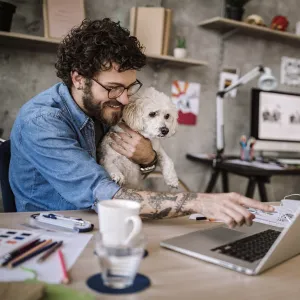 A man working on his laptop with his dog in his lap.