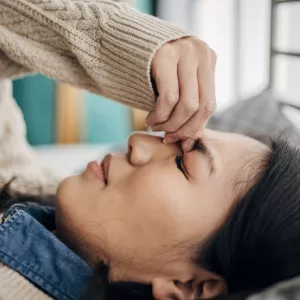 A woman with a headache holds her fingers to the bridge of her nose.