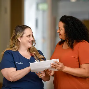 An AdventHealth nurse talking with a female patient while both hold a document.