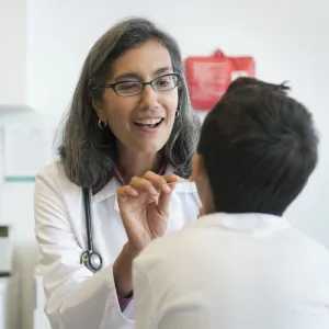 A female doctor looks into a young patient's mouth in an exam room.