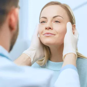 A doctor holds his hands to each side of a woman's face.