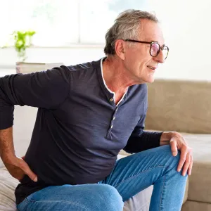 A senior gentleman showing discomfort while getting up from his couch