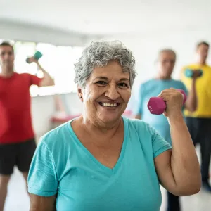 Senior woman smiling and lifting a free weight while in a group exercise class.