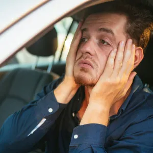 An upset man holds his face with his hands while sitting in a car.