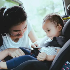 A mother buckles her child into a car seat in the back of a car.