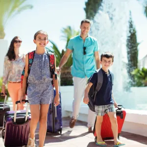A family walks together outdoors with their luggage. 