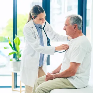 A female physician examining an older man's breathing with a stethoscope. 