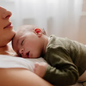 A serene mother cuddles with her sleeping newborn baby.