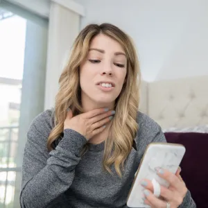 Woman holding throat while on phone