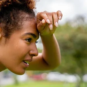 A woman wipes her brow while taking a break from exercising outdoors.