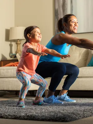 A mother and her young daughter exercise together in the living room.