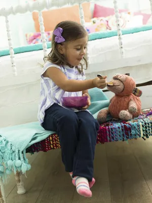 A little girl pretends to feed her stuffed animal in her bedroom