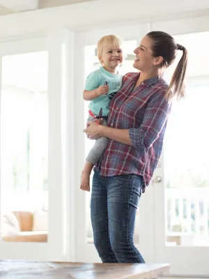 A mom holds her toddler son in a living room full of toys