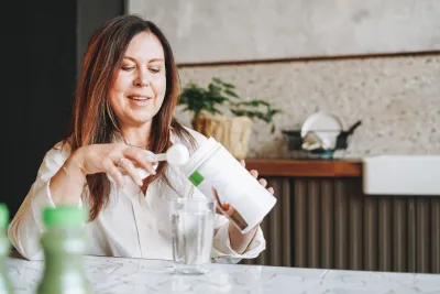 A Woman Scoops Protein Powder from a Container in Her Kitchen.