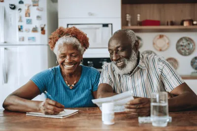 Man and Woman Sitting at Table Tracking Medications in Notebook