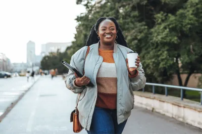 A Woman Walks Down a City Sidewalk with a Cup of Coffee