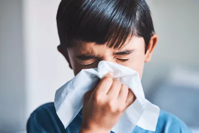 A young boy blowing his nose into a tissue.
