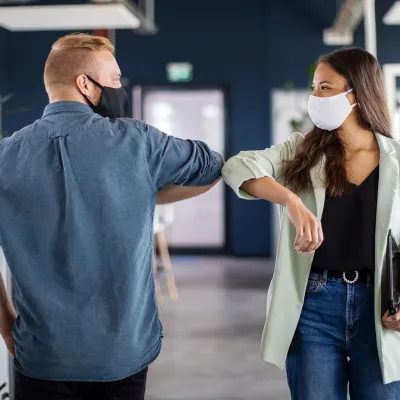 co-workers elbowing hello in the office while wear facemasks