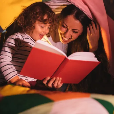 A mom and daughter read together by flashlight.