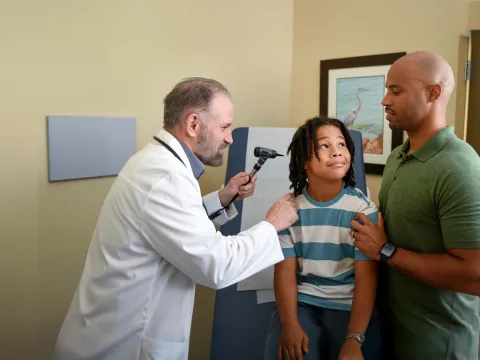 A Centra Care Provider Checks a Child Patient's Ears While His Father Supports Him