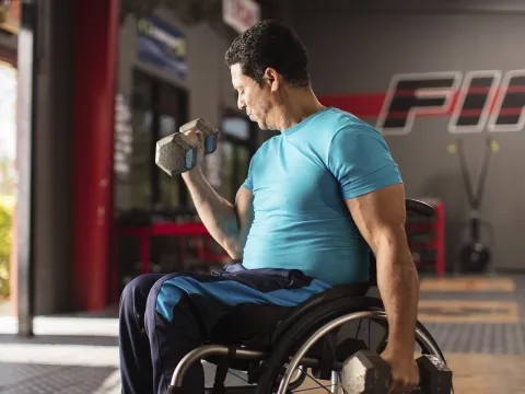 A man in a wheelchair lifts free weights at the gym.