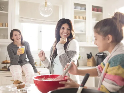 A Caucasian mom dances around the kitchen with her two daughters.