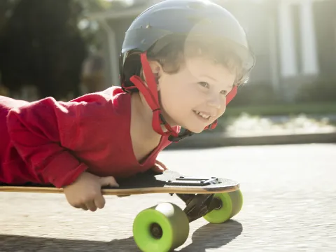 A young boy rides on a skateboard on his belly.