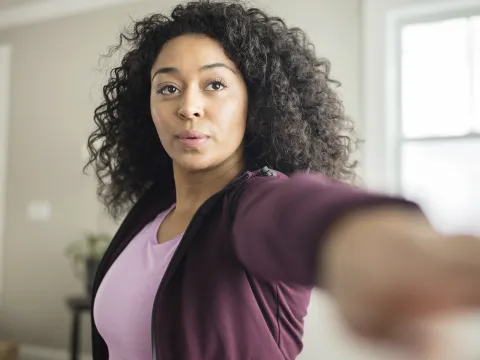 A young African American woman stretches for exercise in her living room.