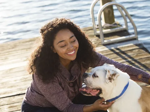 A young African American women plays with her dog on a dock by the lake.