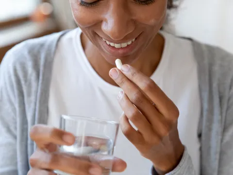 A woman smiles as she's about to take a vitamin.
