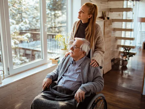 Caregiver Looks Out the Window with a Senior Patient at the Newly Fallen Snow.