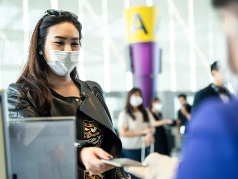Lady checking in for a flight at an airline counter wearing a covid mask