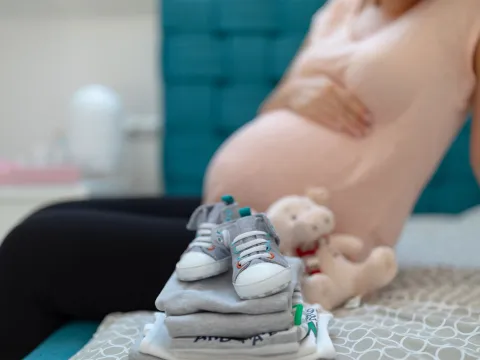 A picture of a set of baby clothes folded next to a pregnant mother