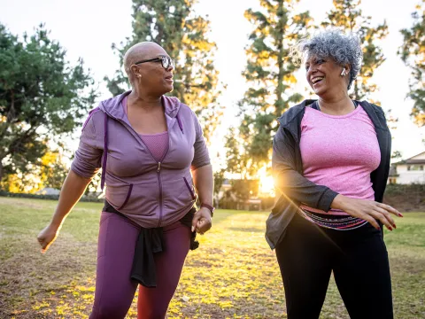 Two Ladies Laugh and Talk as They Walk Through a Park at Sunrise