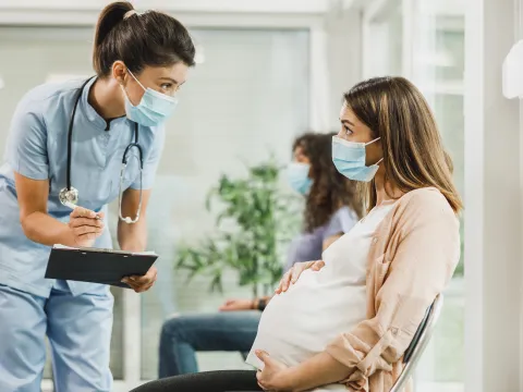 A Care Provider Speaks to a Patient While She Sits in the Waiting Room Holding Her Baby Bump.