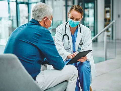 A female physician talking to a grey-haired gentleman with her tablet