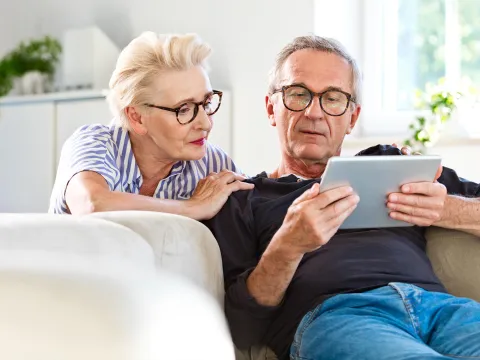 A Senior Couple Looks at a Tablet Together in Their Living Room.