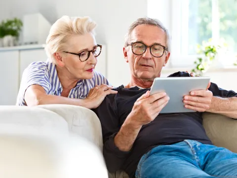 A Senior Couple Looks at a Tablet Together in Their Living Room.