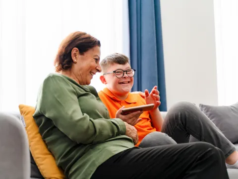 A Child with Down Syndrome Smiles While he and his Mother Look at Content on an iPad