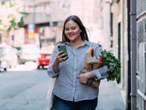A Woman Walks Down the Sidewalk Checking Her Phone While Carrying Groceries