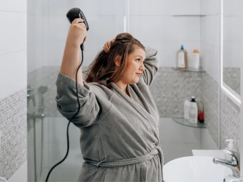 A Woman Blow Dries Her Hair in the Bathroom Mirror
