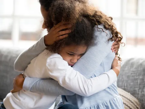 A Mother Hugs Her Sad Daughter on the Couch at Home.