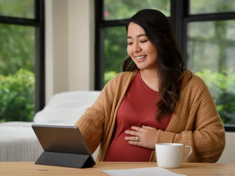 A Pregnant Woman Smiles as She Uses a Tablet at Home