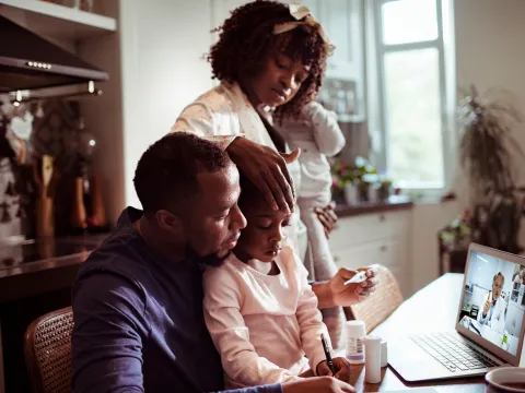 A Family Huddles Around a Laptop to Participate in a Video Visit with a Physician.