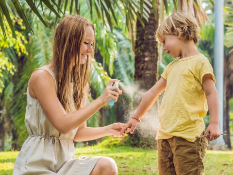 A Mother Sprays Her Young Son with Bug Spray in a Park