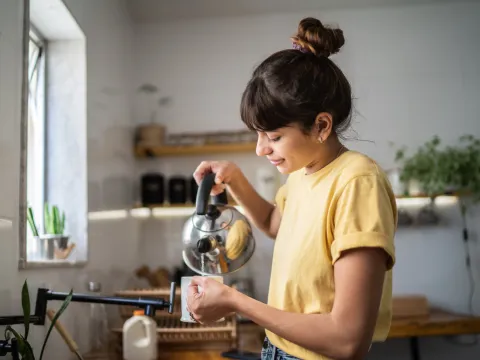 A Woman Smiles as She Pour Hot Water from a Tea Kettle into a Cup