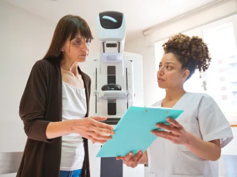 A Woman and a Provider Go Over a Chart in Front of Mammogram Machine