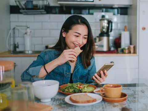 A Woman Smile at Her Mobile Device as She Eats a Balanced Breakfast