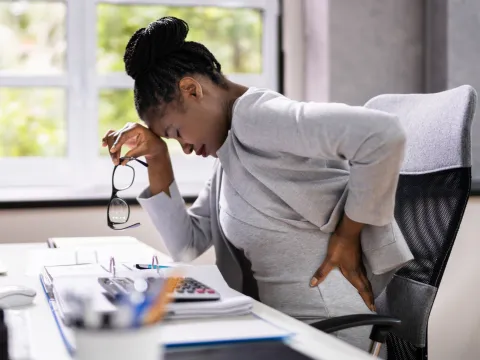 A Woman Sitting at Computer Leans Forward Because of Back Pain