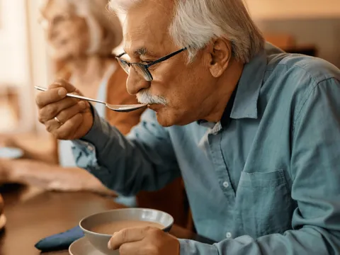 A Senior Man Eats Soup at the Dinning Room Table with Family